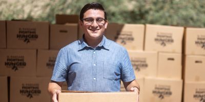 A smiling young man standing in front of many food boxes.