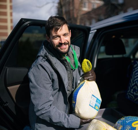 A man holding a frozen turkey in front of an open car.