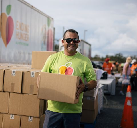 A man holding a box and smiling in front of a pallet of boxes.